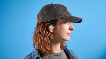 Weiße Denon PerL Pro True-Wireless-Ohrhörer mit rundem Design und passender Ladehülle vor blauem Hintergrund