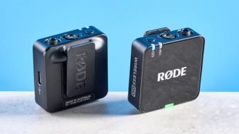 Das Rode Wireless GO Gen 3 Mikrofonsystem mit einem Empfänger und zwei Sendern, präsentiert mit Fellwindschützen, Ladeanschlüssen und Kabeln auf blauem Hintergrund