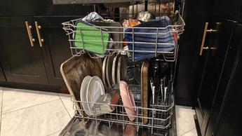 Mesin pencuci piring Whirlpool WDT750SAKZ dalam keadaan terbuka dengan piring penuh di dapur modern berkabinet hitam dan lantai keramik.
