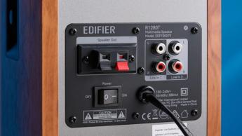 Die Edifier R1280T Regallautsprecher in Holzbraun auf blauem Hintergrund, mit Fokus auf Lautstärkeregler, Lautsprecherchassis, Hochtöner, RCA- und AUX-Anschlüsse sowie Fernbedienung