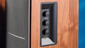 Die Edifier R1280T Regallautsprecher in Holzoptik vor blauem Hintergrund, mit hervorgehobenen Lautstärkereglern, Lautsprechertreibern, Hochtönern, RCA- und AUX-Anschlüssen sowie der mitgelieferten Fernbedienung