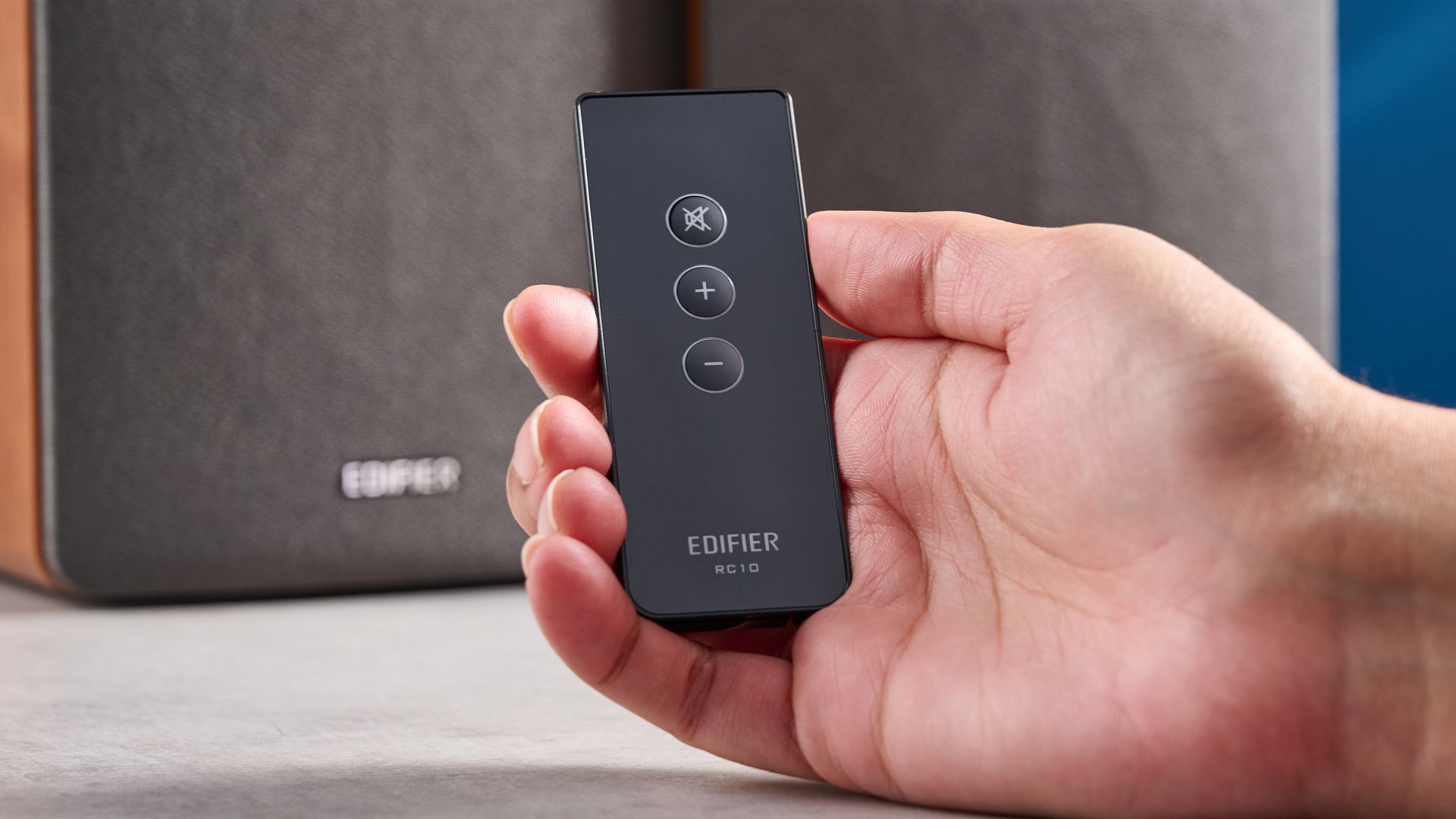 Die Edifier R1280T Regallautsprecher im Holzfurnier vor blauem Hintergrund, mit Fokus auf die Lautstärkeregler, die Lautsprechertreiber, den Hochtöner, die RCA- und AUX-Eingänge sowie die Fernbedienung