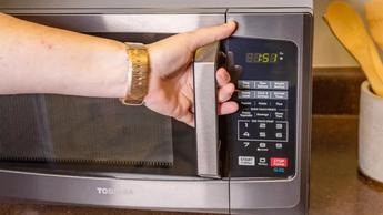 Persona abriendo la puerta de un microondas Toshiba EM925A5A-BS