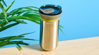 Cafeteira pour-over Wacaco Cuppamoka de inox com filtros de papel marrom e tampa para beber, sobre fundo azul