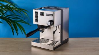 Máquina de espresso Rancilio Silvia em aço inoxidável sobre uma bancada de madeira com parede azul ao fundo