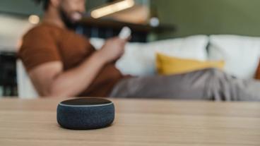 Joven afroamericano relajándose en el sofá, usando su smartphone con un altavoz inteligente sobre la mesa del salón