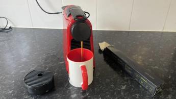 Cafetera Nespresso Essenza Mini preparando café fresco en una taza roja con blanco
