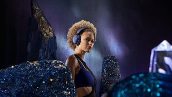 Uma mulher usando os fones de ouvido Bose QuietComfort Ultra na cor violeta escuro, cercada por cristais roxos