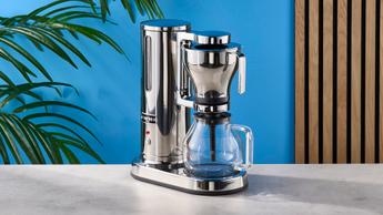 uma cafeteira de filtro de aço inox com capacidade para 10 xícaras exibida contra um fundo azul