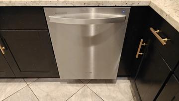 Lavavajillas Whirlpool de acero inoxidable instalado con gabinetes de cocina negros, cubierta de mármol y piso de loseta