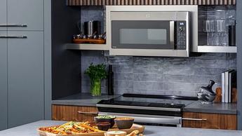 Microondas de convección GE Profile instalado sobre la estufa en una cocina moderna de color gris oscuro