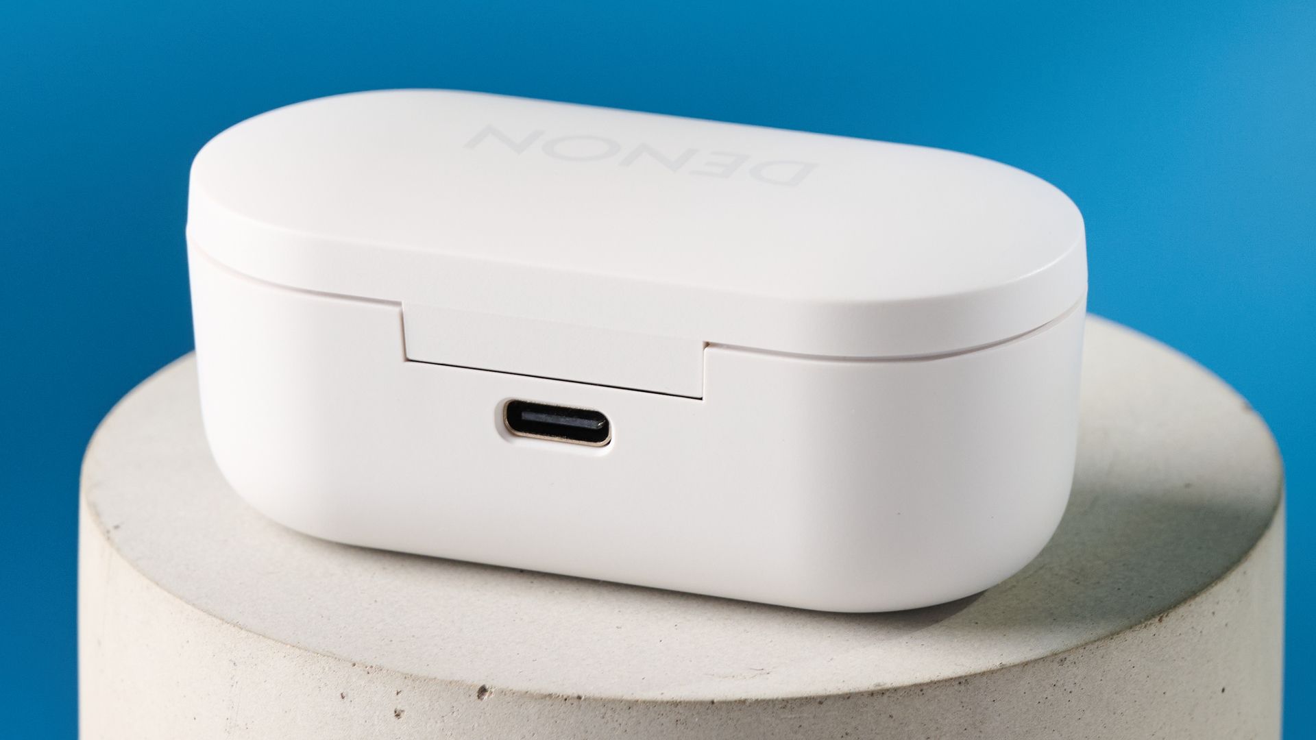Denon PerL Pro True-Wireless-Ohrhörer in Weiß mit rundem Design und passender weißer Ladehülle auf blauem Hintergrund