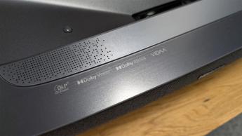 Крупный план края ультракороткофокусного проектора Hisense PL2 с логотипами бренда и решёткой динамика