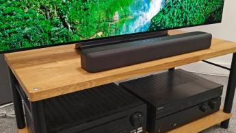 Саундбар Amazon Fire TV, установленный на деревянной стойке для аудио- и видеотехники, с другой аппаратурой на полке ниже
