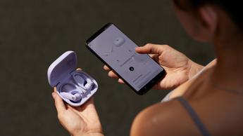 En kvinde holder Beats Powerbeats Pro 2 trådløse øretelefoner og en smartphone, der viser ledsager-appen med mulighed for at slå pulsmåling til