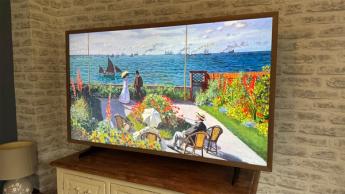 Hisense Canvas 55-inch TV on wooden chest of drawers in front of brick wall with wood-effect frame attached and colourful painting on screen