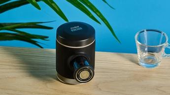 A cafeteira portátil Wacaco Picopresso sobre uma superfície de madeira com um copo de espresso ao lado