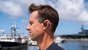 En mand lytter til musik med JLab Epic Open Sport-øretelefoner ved en havn
