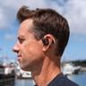 Un uomo ascolta musica con gli auricolari JLab Epic Open Sport vicino a un porto turistico