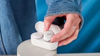 Denon PerL Pro True-Wireless-Ohrhörer in Weiß mit kreisförmigem Design und passendem Ladecase vor blauem Hintergrund