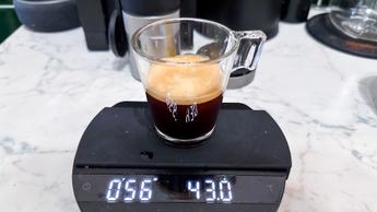 Um café espresso fresco sendo servido em um copo de vidro sobre uma balança digital de café