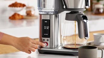 Pessoa pressionando um botão na interface da cafeteira Breville Luxe Brewer