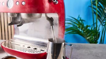 Uma máquina de espresso vermelha da Smeg com moedor de grãos integrado, sobre um fundo azul