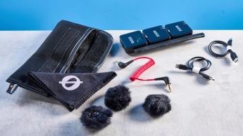 Das Rode Wireless GO Gen 3 Mikrofon-Set mit einem Empfänger, zwei Sendern sowie Zubehör wie Deadcat-Windschutz, Ladeanschlüssen und Kabeln auf blauem Hintergrund