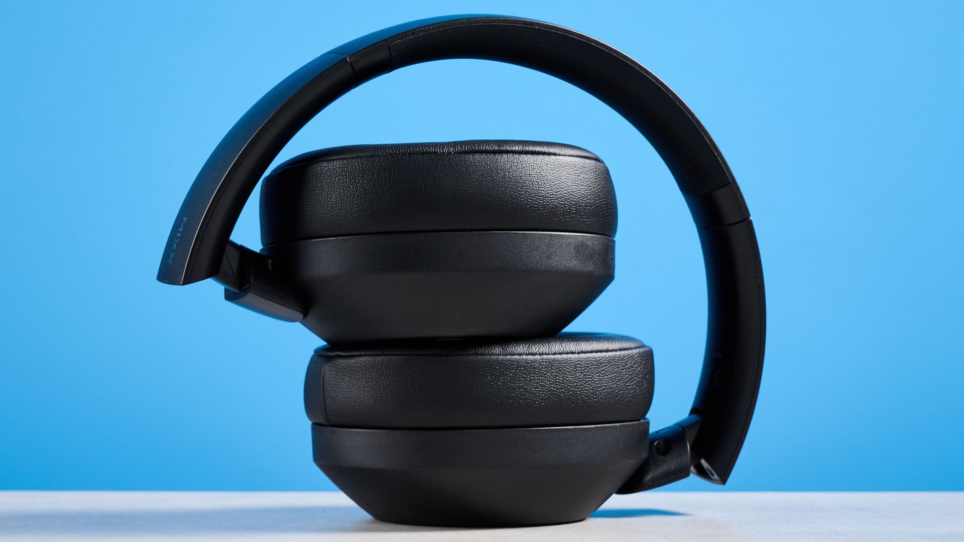 Mixx StreamQ C4 kabellose Kopfhörer in Schwarz mit weichen Ohrpolstern und sichtbaren Bedientasten vor blauem Hintergrund