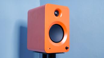 Ein orangefarbener Kanto Ren Aktivlautsprecher auf einem Ständer vor einer blauen Wand