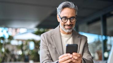 Um homem de cabelo prateado olhando com alegria para seu smartphone, interagindo com seu dispositivo móvel.