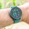 Primer plano de un smartwatch Garmin Vivoactive 6 verde en la muñeca de una persona, con follaje verde desenfocado al fondo