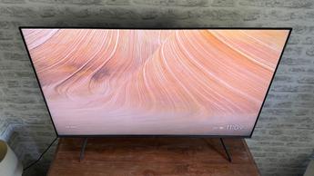 Смарт-телевизор TCL C6KS с диагональю 50 дюймов на фоне кирпичной стены, на экране — яркое изображение пустыни с закрученными узорами