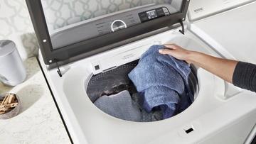 Personne plaçant une serviette bleue dans une machine à laver Maytag MVW7232HW à chargement par le haut