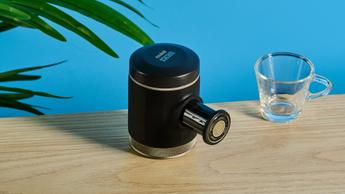 A cafeteira portátil Wacaco Picopresso sobre uma mesa de madeira, ao lado um copo de espresso