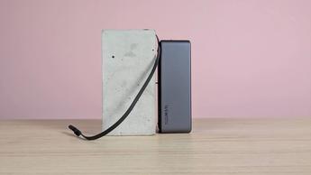 Batería externa Ugreen Nexode de 20.000 mAh y 165 W con cable USB-C integrado, sobre un pedestal en un escritorio con fondo rosa