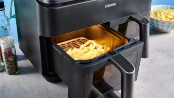 Uma fritadeira elétrica Cosori preta com dois cestos, janelas transparentes, luzes internas, grelha para cozimento e espetos para churrasco