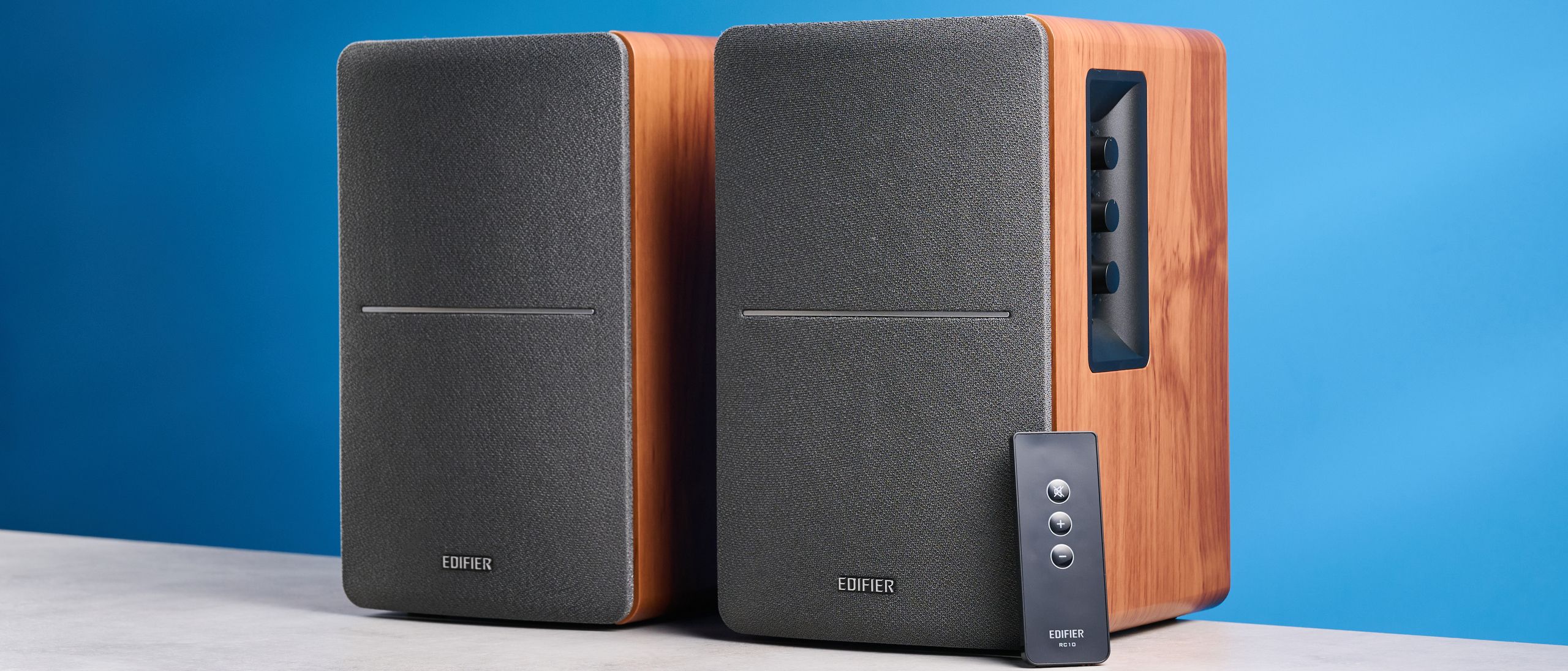 Edifier r1280t Regallautsprecher in Holzoptik Braun mit sichtbaren Lautstärkereglern, Treibern, Hochtönern, RCA- und AUX-Eingängen sowie Fernbedienung vor blauem Hintergrund