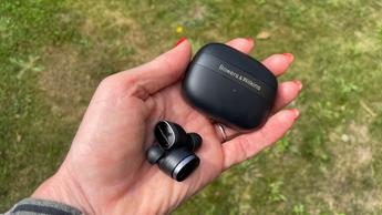 Bowers & Wilkins Pi8 trådløse øretelefoner holdt i hånden med grøn græsbaggrund