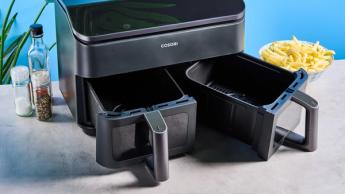 Uma fritadeira elétrica Cosori preta com cestos duplos transparentes, luzes internas, grelha para cozimento e espetos para churrasco