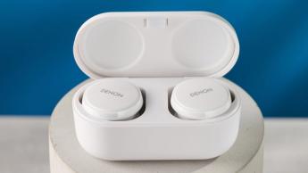 Weiße Denon perL Pro True-Wireless-Ohrhörer mit rundem Design und passendem Ladeetui vor blauem Hintergrund