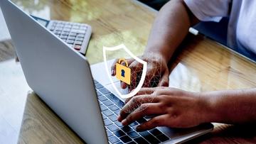Händer som skriver på ett laptop-tangentbord med en säkerhetslåssymbol på skärmen