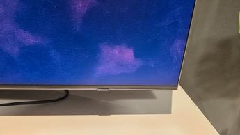 Samsung QN990F on a white media unit with a grey curtain in the behind it and soundbar in front