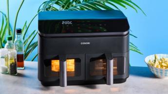 Uma fritadeira elétrica Cosori preta com dois cestos transparentes, luzes internas, grelha para cozimento e espetos para churrasco