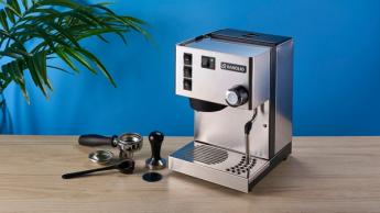 Máquina de espresso Rancilio Silvia em aço inox sobre uma bancada de madeira com uma parede azul ao fundo