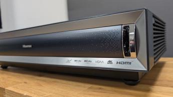 Короткофокусный проектор Hisense PX3 на деревянной стойке в современной гостиной с белыми и серыми стенами