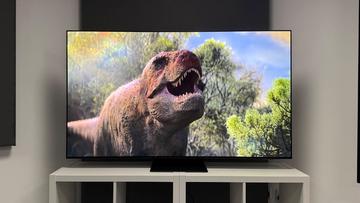 OLED-телевизор Samsung S95F с изображением ти-рекса на экране, установлен на белой деревянной мебели