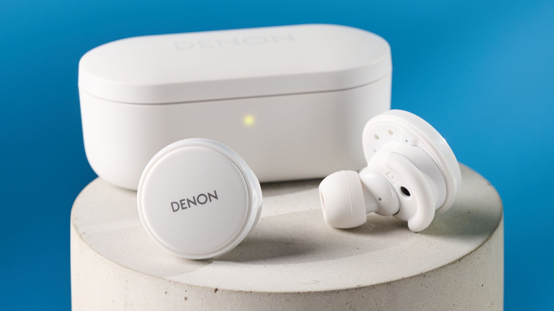 Weiße Denon perL Pro kabellose Ohrhörer mit rundem Design und passender Ladehülle vor blauem Hintergrund