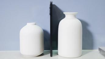 Samsung Galaxy S25 Edge in black against a blue background with two white vases