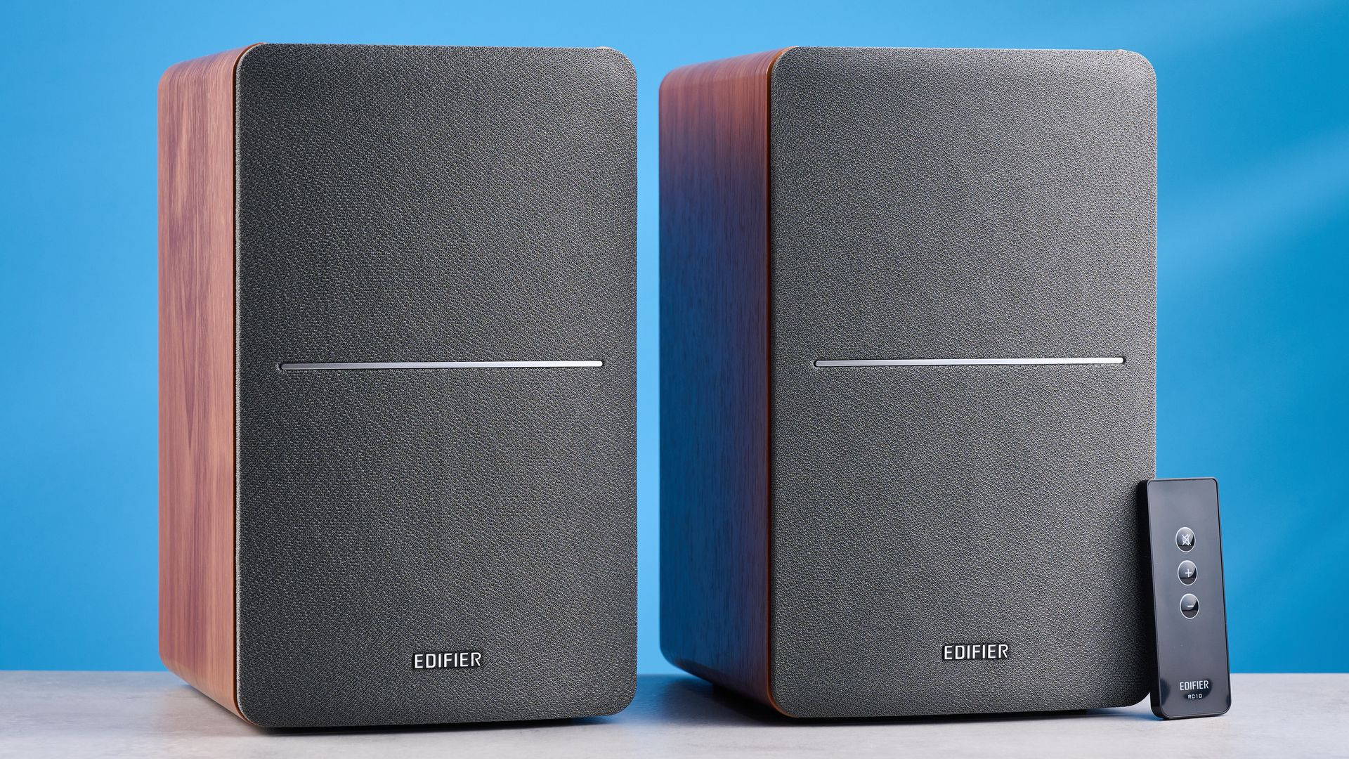 Die Edifier R1280T Regallautsprecher in Holzoptik vor blauem Hintergrund, mit sichtbaren Lautstärkereglern, Treibern, Hochtönern, RCA- und AUX-Eingängen sowie Fernbedienung.